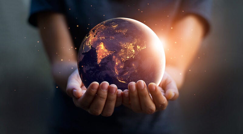 An image of a person's arms and hands holding a globe. The globe is made to glow as if sunlight is washing over it.