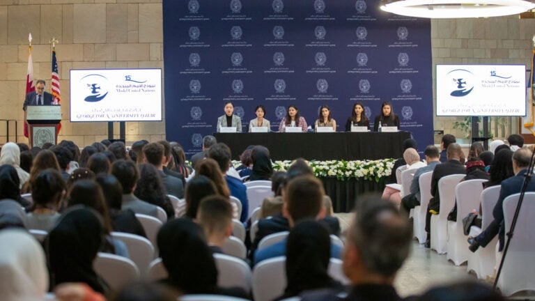 Students seated on stage in a conference room for a Model United Nations conference with a full audience watching.
