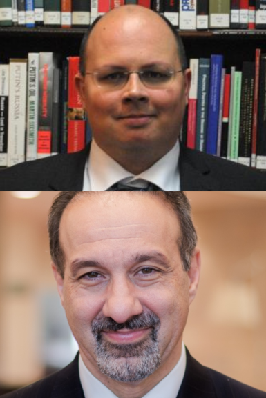 Two men in suits: the first is bald and wears glasses, standing in front of bookshelves; the second has short dark hair, a goatee, and is smiling in front of a blurred indoor background.