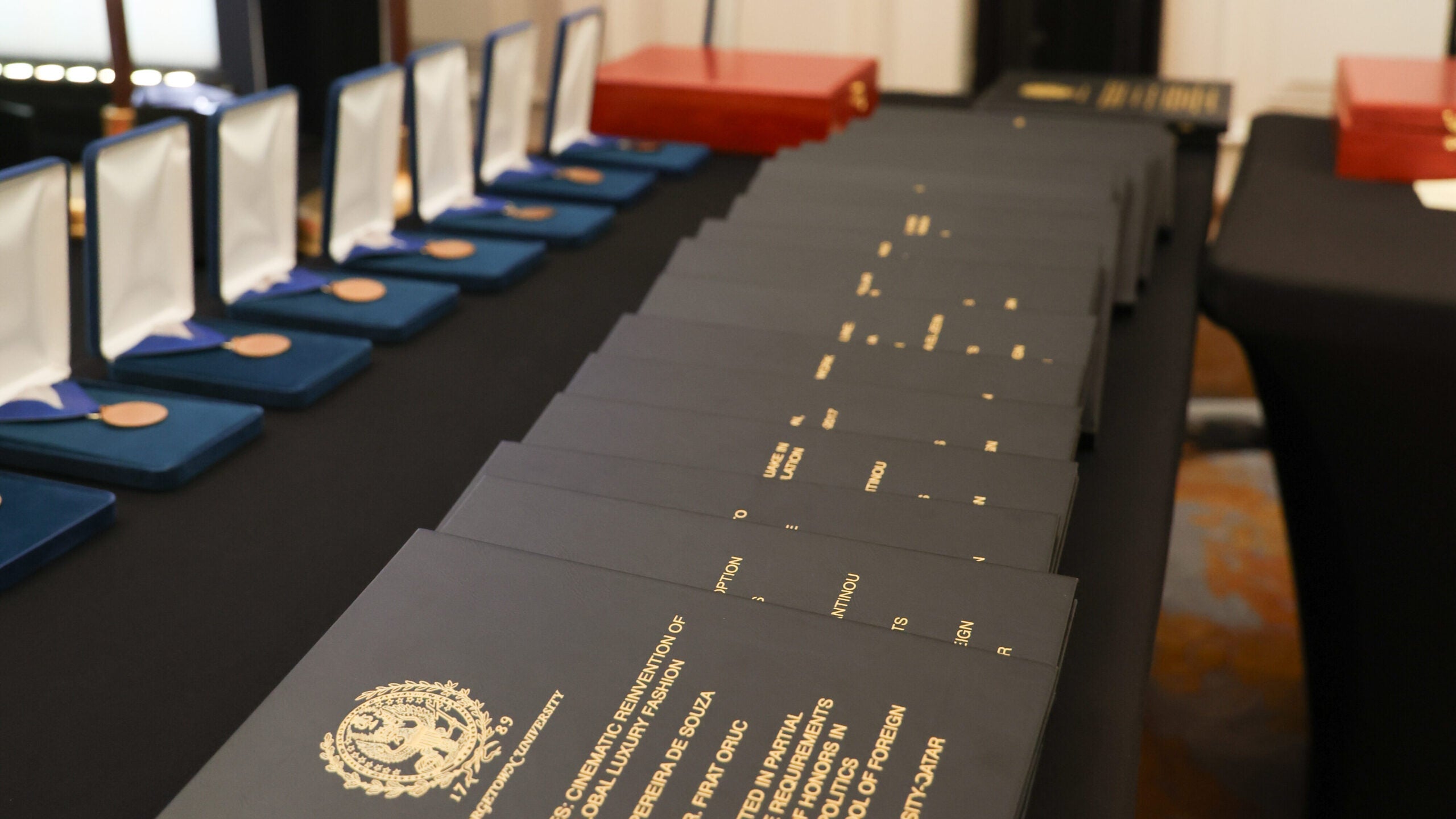 Several certificates and medals displayed on a black table at an award ceremony, with official emblems visible on the documents and medals arranged in blue cases.