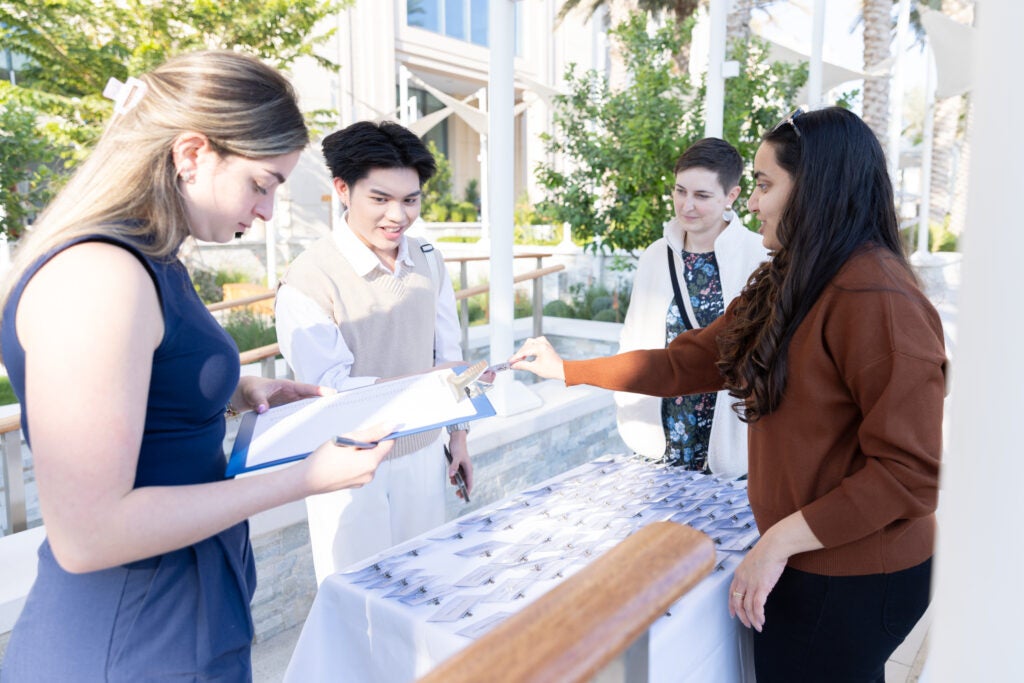Students pick up name tags from a table at an outdoor event.